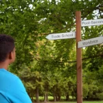 A youth standing and observing a crossroad sign.