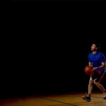 A basketball player on a dark court, about to shoot the ball.