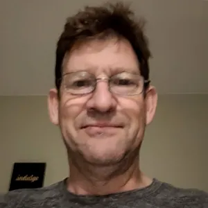 A man wearing glasses and a gray shirt takes a selfie.